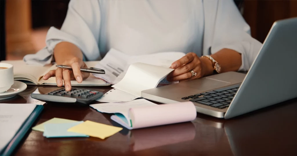 Mindestlohn berechnen: Vorgaben für Arbeitgeber und Lohnabrechnung Mindestlohn Berechnung mit Taschenrechner, Laptop und Unterlagen