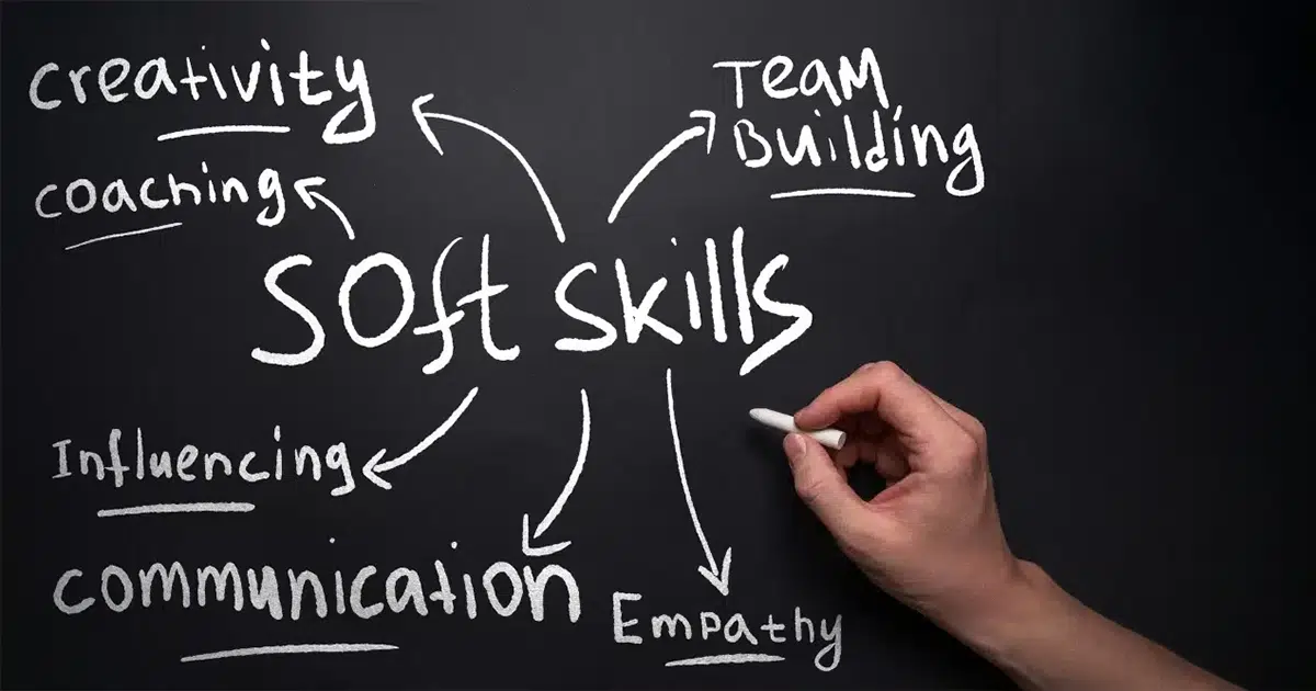 Soft Skills Beispiele werden mit Kreide auf eine schwarze Tafel geschrieben Soft-Skills: Auf einer schwarzen Tafel schreibt eine Hand mit Kreide Soft Skills Beispiele auf