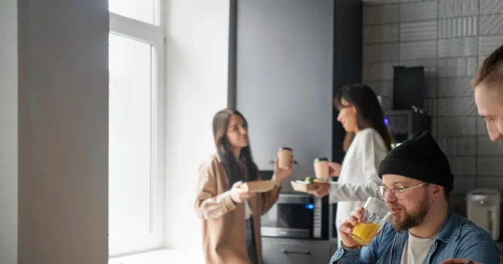 Gesetzliche Pausenzeit – Mitarbeitende entspannen in der Büroküche Mitarbeitende machen Pause in der Büroküche – gesetzliche Pausenregelung im Unternehmen