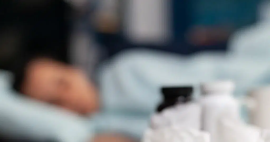 Krankschreibung rückwirkend, Erkrankte Person liegt im Bett, Medikamente im Vordergrund