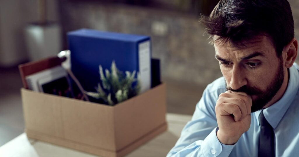 Kündigungsfrist und Jobverlust – Mann sitzt nach Kündigung nachdenklich neben Umzugskarton