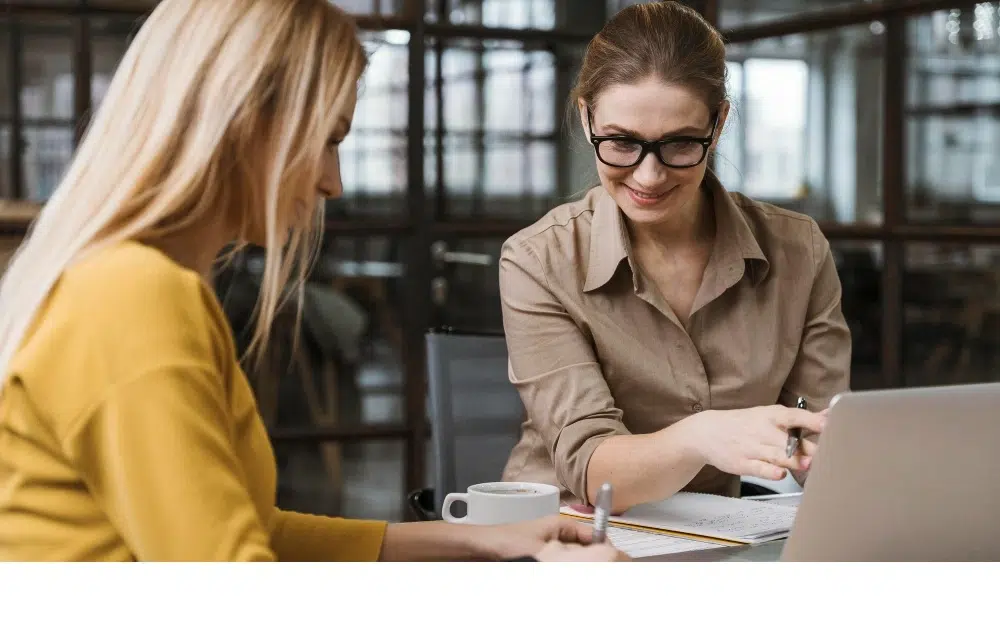 Mitarbeitergespräch zwischen zwei Frauen im Büro mit Laptop und Unterlagen