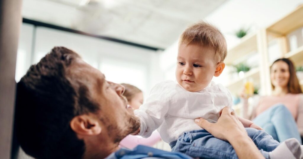 Vater spielt zuhause mit seinem Baby während des Vaterschaftsurlaubs