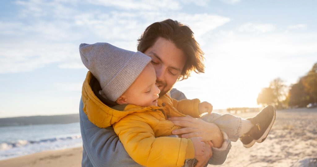 Vater hält sein Kleinkind am Strand während des Vaterschaftsurlaubs