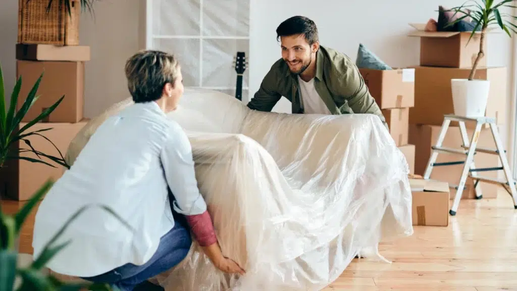 Zwei Personen tragen ein in Folie verpacktes Sofa in eine neue Wohnung