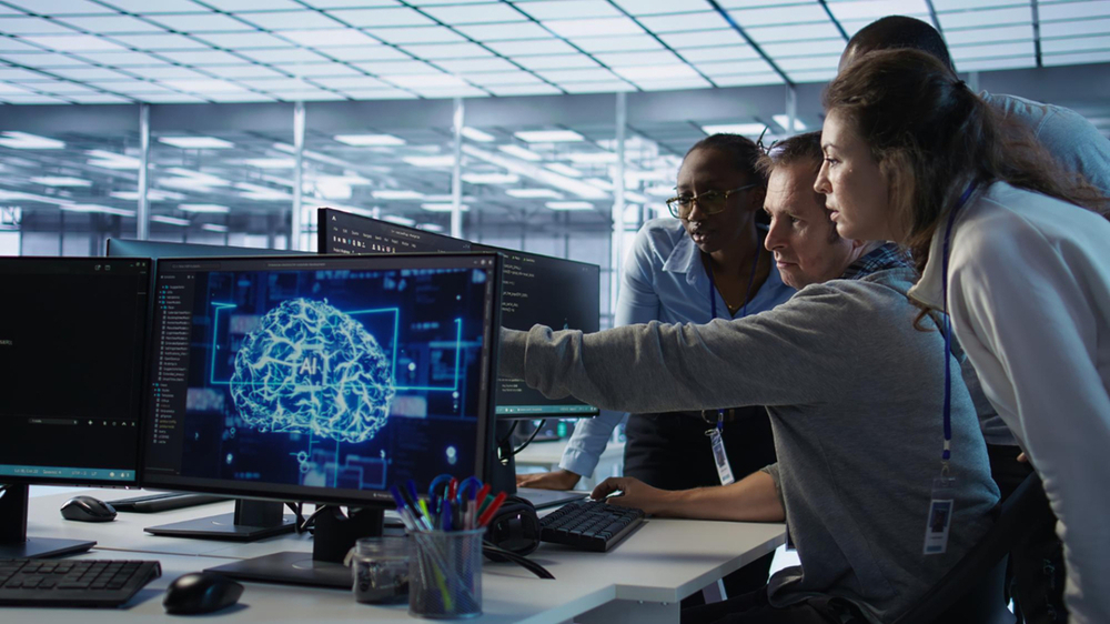 Human-in-the-Loop: KI-Prozesse mittels menschlicher Kontrolle Human-in-the-Loop: Zwei Mitarbeiterinnen nutzen KI- und VR-Technologie am Büroschreibtisch