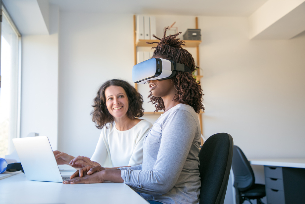 Human-in-the-Loop: KI-Prozesse mithilfe menschlicher Kontrolle Human-in-the-Loop: Zwei Mitarbeiterinnen nutzen KI- und VR-Technologie am Büroschreibtisch