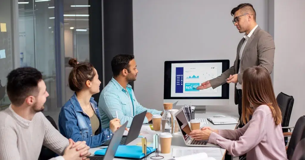 HRMS-System für HR-Analysen und Personalprozesse HRMS-System zeigt Auswertung von Personalprozessen in einer Teampräsentation am Bildschirm