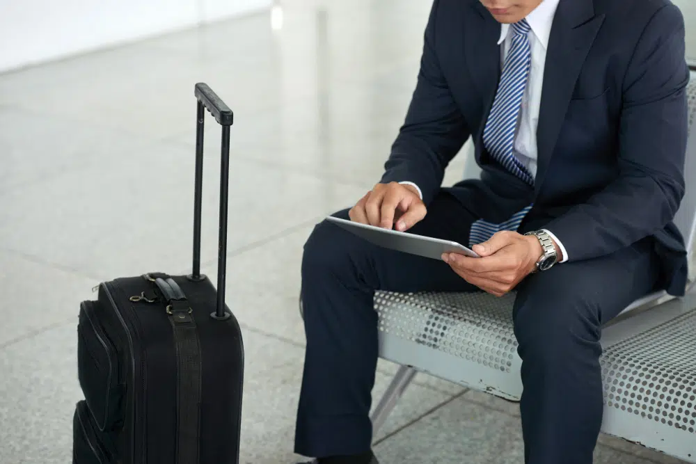 Geschäftsmann auf Reisen erstellt auf einem Tablet seine digitale Reisekostenabrechnung Geschäftsperson mit Tablet und Koffer bei der digitalen Reisekostenabrechnung
